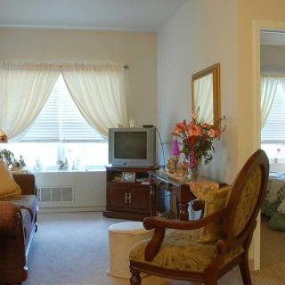 A cozy living room with classic furnishings, featuring a TV, floral arrangements, and elegant curtains.