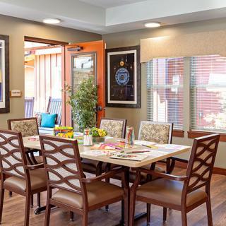 A well-decorated dining room featuring a large table surrounded by chairs, with artwork on the walls and plenty of natural light.