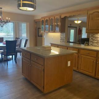 A spacious open kitchen with wooden cabinets and an island, adjacent to a dining area with a chandelier.
