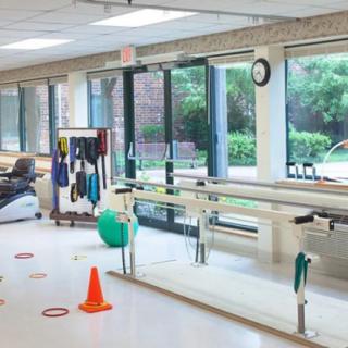 A well-lit physical therapy clinic equipped with parallel bars and various exercise tools.