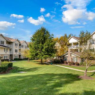 A scenic view of a residential apartment complex with well-maintained green spaces and trees under a clear blue sky.