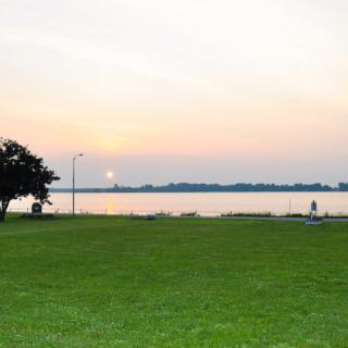 A serene lakeside park at sunset with a clear sky and vibrant greenery.