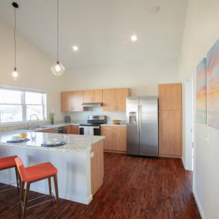 A modern kitchen with stainless steel appliances, wood flooring, and an open-concept design featuring a kitchen island with bar stools.