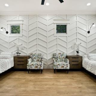 A modern bedroom with twin beds, nightstands, and armchairs, featuring wood flooring and stylish wall decor.