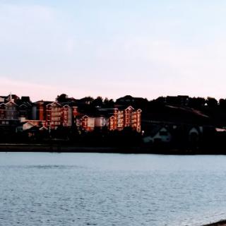 A serene view of a waterfront cityscape at sunset, where the buildings reflect the warm hues of the sky.