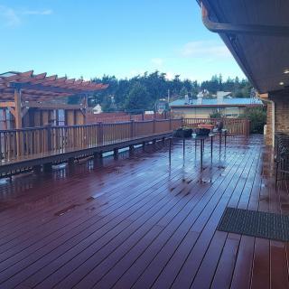 A spacious wooden deck with benches and tables, set against a backdrop of trees under a clear sky.