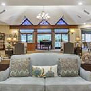 A spacious living room with a sofa, decorative pillows, large windows, and a chandelier.