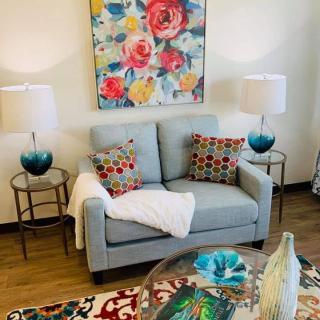 A cozy living room with a light blue sofa, vibrant floral painting, and colorful decorative accents.