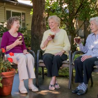 Three seniors enjoying drinks and conversation in a garden setting.