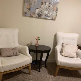 A cozy corner with two white armchairs, a small round table, and a wall painting.