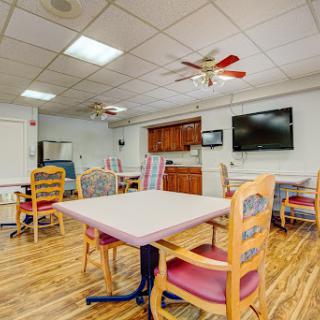 A spacious dining area featuring several tables and chairs, with a kitchenette and a television on the wall.