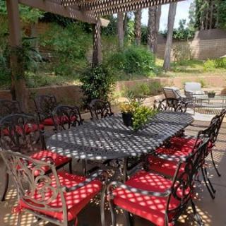 A beautifully arranged outdoor patio with a large table and red-cushioned chairs under a pergola.