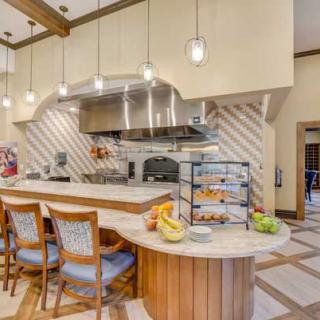A modern kitchen interior with a central counter and bar stools, featuring hanging lights and cooking equipment.