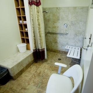 An accessible bathroom featuring a wheelchair-friendly shower with handrails and a foldable seat.