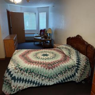 A cozy bedroom with a colorful quilt on the bed and natural light coming in through the windows.