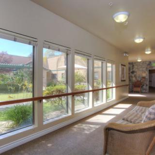 A well-lit hallway with large windows offering a view of the garden, featuring a comfortable sofa along one side.