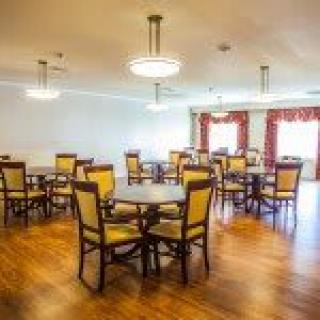 A spacious dining room with multiple tables and chairs, featuring elegant lighting and hardwood flooring.