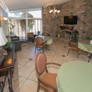 A cozy dining area with tables and chairs, featuring a stone wall, large windows, and a television.