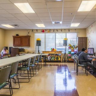 A classroom with desks, chairs, and computers, with people working inside.