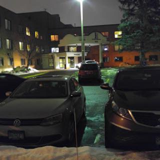 A quiet parking lot at night, illuminated by a streetlight, with parked cars and snow on the ground.