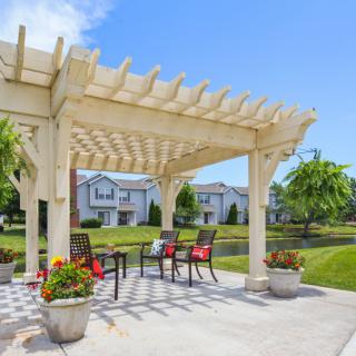 A welcoming outdoor patio with a wooden pergola, surrounded by a garden and vibrant flowers.