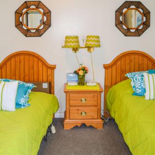 A cozy bedroom with two twin beds featuring wooden headboards, vibrant pillows, and a central nightstand adorned with decorative lamps and mirrors.