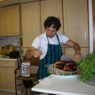 A person in a kitchen carving a roasted turkey.