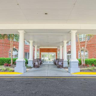 A covered building entrance with columns and a brick facade, surrounded by landscaping.