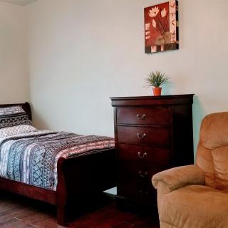 A cozy bedroom featuring a single bed, dark wood dresser, and comfortable armchair.