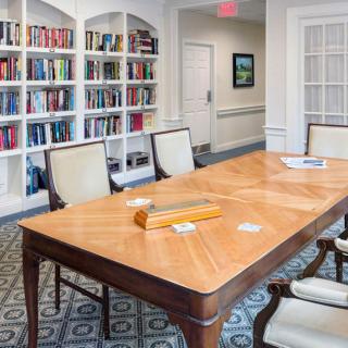 A well-furnished meeting room featuring a large wooden table surrounded by chairs, with bookshelves lining the walls.