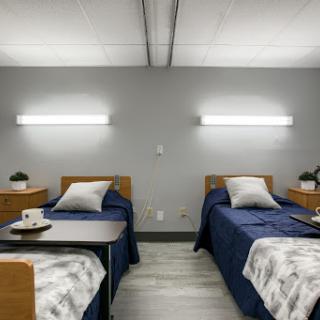 A modern, well-lit shared bedroom featuring two neatly made beds with blue bedspreads.