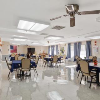 A community dining area with tables and chairs, featuring a ceiling fan and American flag.
