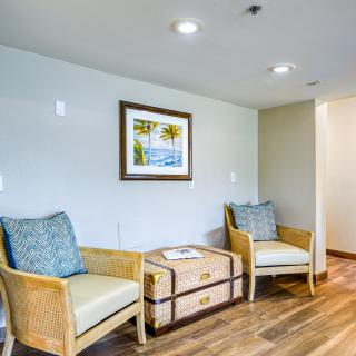 A cozy lounge area with two wicker chairs and a decorative chest, complemented by a framed beach scene on the wall.