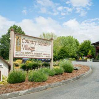 Entrance sign to Country Village surrounded by landscaped greenery and a paved driveway.