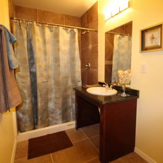 A well-lit bathroom featuring a shower with a curtain, a sink with a vanity, and neatly hung towels.