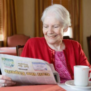 An elderly woman enjoying a newspaper with a cup of coffee indoors.