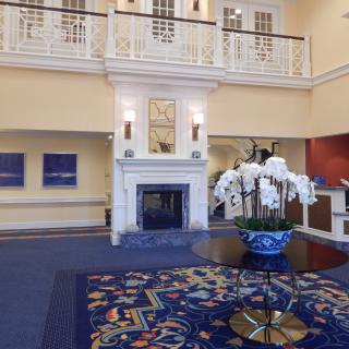 A stylish hotel lobby with a central table featuring an orchid arrangement and a grand fireplace.
