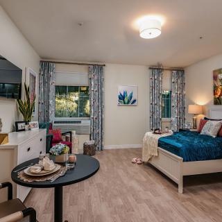 A stylish and cozy bedroom with modern decor, featuring a comfortable bed, a small dining table, and vibrant artwork.