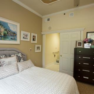 A cozy bedroom with a neatly made bed, artwork on the walls, and a dark wooden dresser.