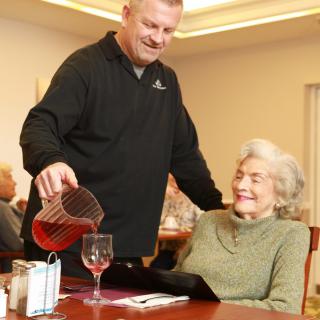A man is pouring a drink for an elderly woman in a restaurant setting.