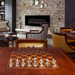 A cozy living room featuring a chessboard ready for play, with comfortable seating and a stone fireplace.