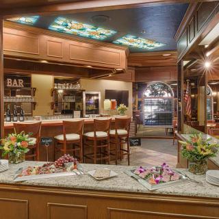 A cozy and elegantly decorated bar with a marble countertop, surrounded by wooden chairs and floral arrangements.