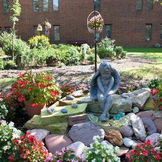 A serene garden setting featuring a thoughtful statue surrounded by vibrant flowers and decorative rocks.