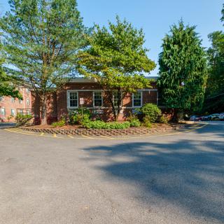 A brick house surrounded by trees and landscaping with a driveway in a suburban setting.