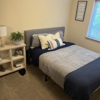 A cozy and neatly arranged bedroom featuring a bed, decorative pillows, and a stylish shelf.