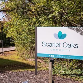 A sign for Scarlet Oaks Academy stands near a tree-lined pathway.