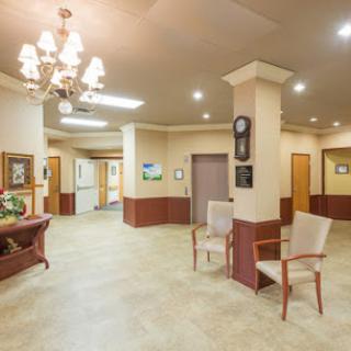 A spacious lobby with elegant furnishings, featuring chairs, a chandelier, and hallway access.