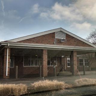 An exterior view of a brick building under a cloudy sky, showcasing its abandoned state.