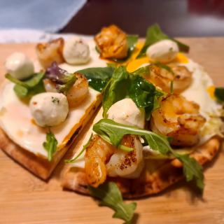 A gourmet pizza topped with shrimp, arugula, and mozzarella balls.