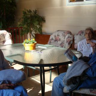 A group of people seated around a glass patio table on a sunny day.